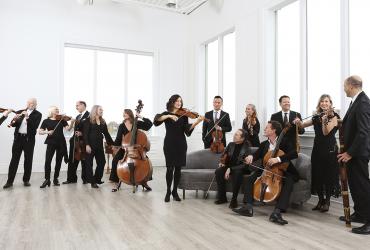 Tafelmusik Baroque Orchestra: musicians standing and playing in a white room